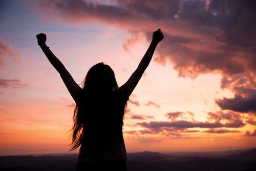 Sihlouette of a woman with her hands in the air cheering by a cliffside