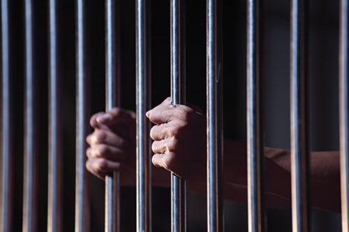Hands holding on to the bars of a prison door
